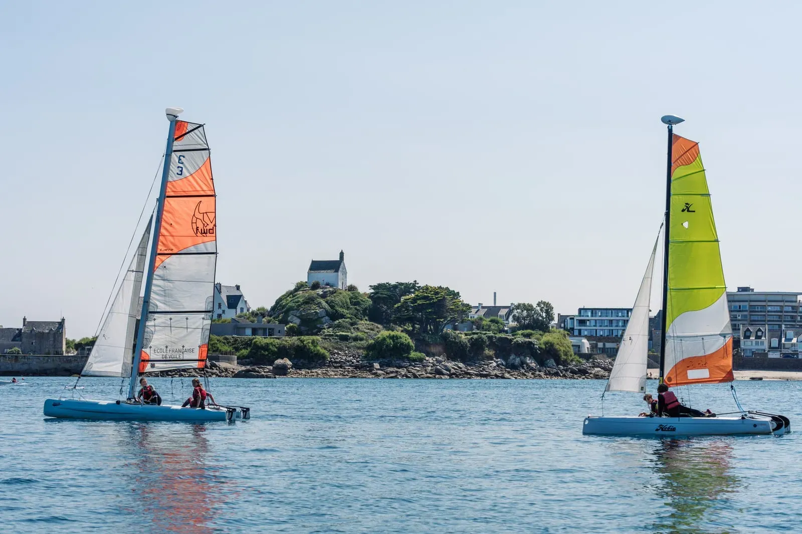 Deux catamarans du club naviguent devant la chapelle Sainte-Barbe, à Roscoff